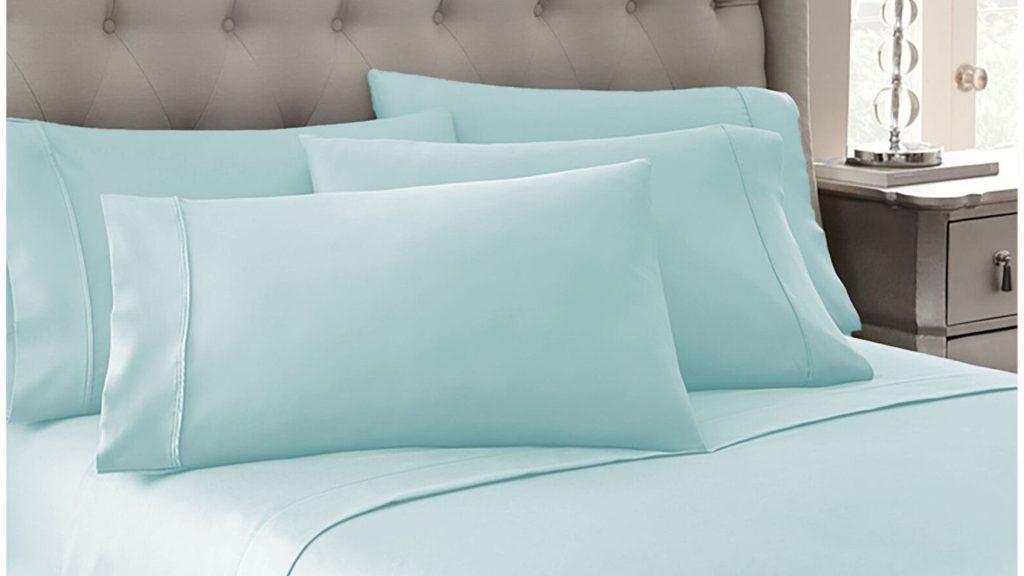 A clean aqua color bedset with deep pocket sheets placed on it alongwith pillows
